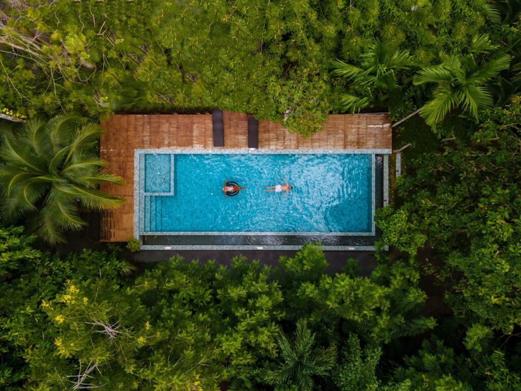 Vista aerea di una coppia che nuota in una piscina immersa nella natura tropicale. Esperienza di viaggio esclusiva Monica Alberghini