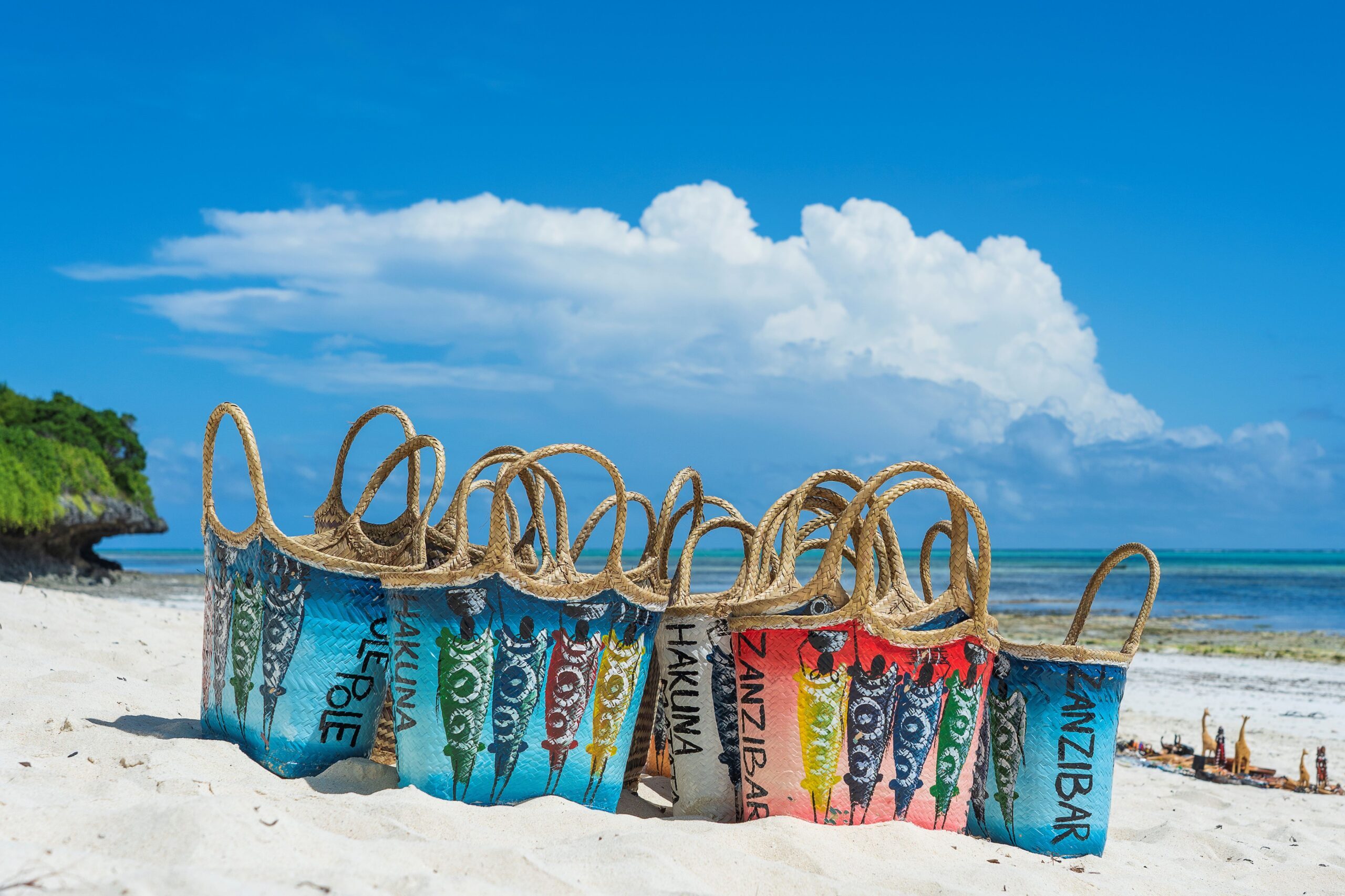 Spiaggia di Zanzibar con borse artigianali colorate in primo piano, proposta di viaggio su misura di Monica Alberghini.