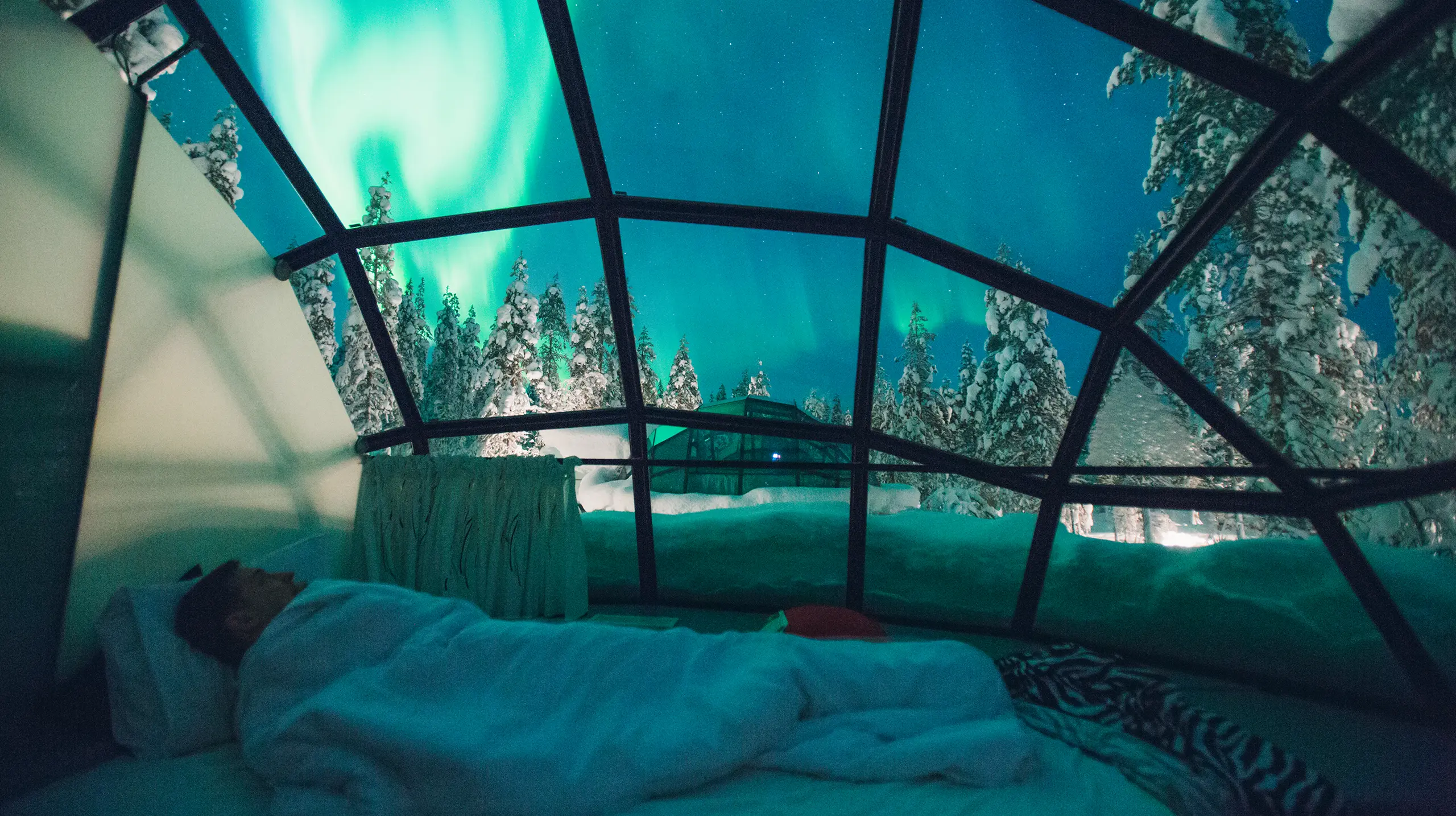 Vista dell'aurora boreale da un igloo di vetro, con un letto al centro e una visuale spettacolare del cielo, esperienza viaggio Monica Alberghini.