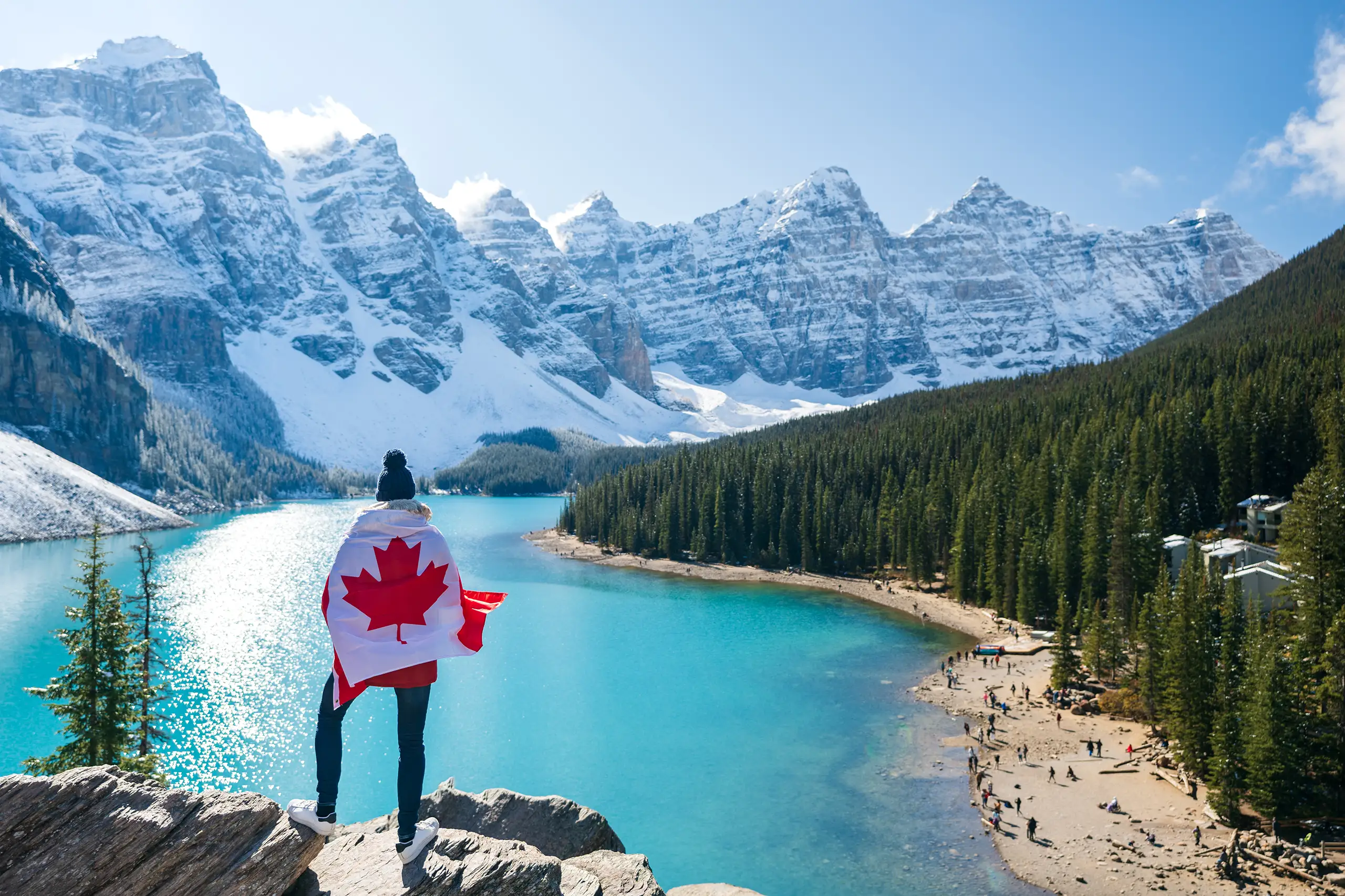 Viaggiatore avvolto in una bandiera canadese osserva il Moraine Lake con le Montagne Rocciose innevate sullo sfondo, Monica Alberghini viaggi