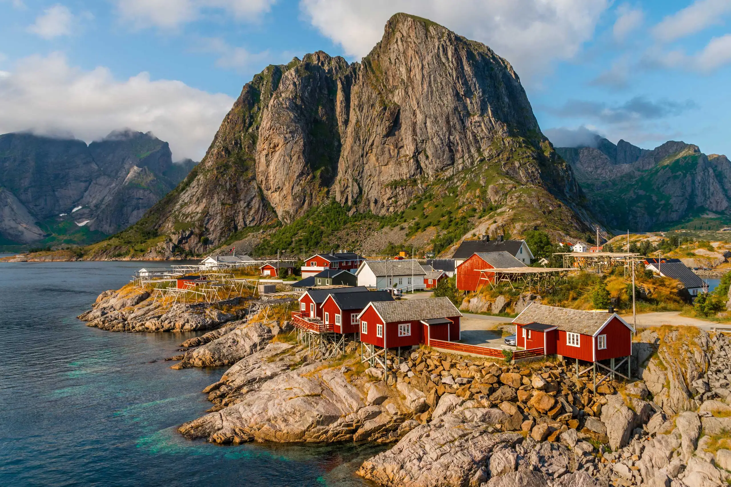 Villaggio di case rosse su una scogliera con montagne sullo sfondo, proposta di viaggio in Norvegia di Monica Alberghini alla scoperta della costa.