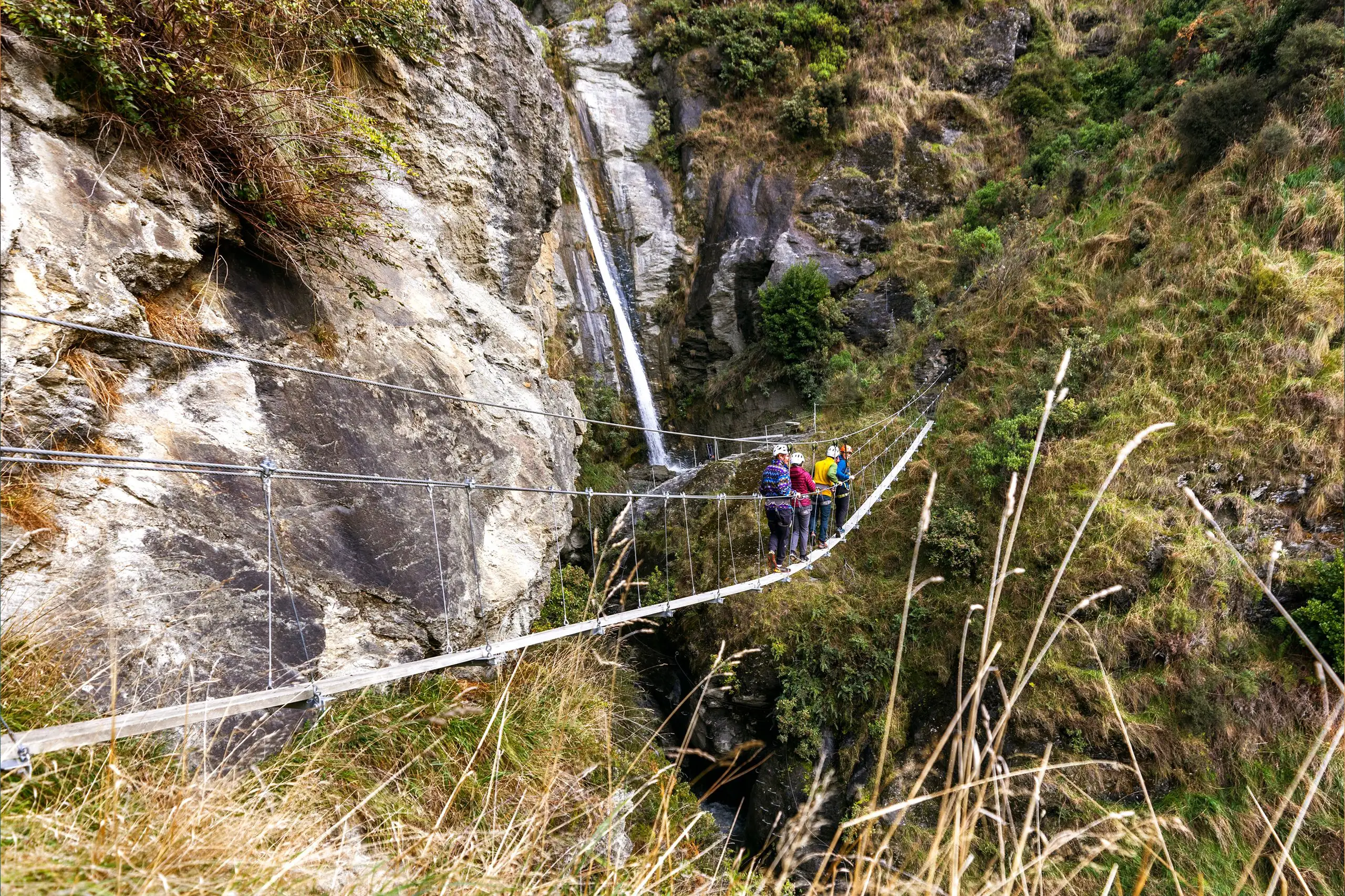 Escursionisti su un ponte sospeso in montagna vicino a una cascata, proposta di viaggio individuale in Nuova Zelanda di Monica Alberghini.