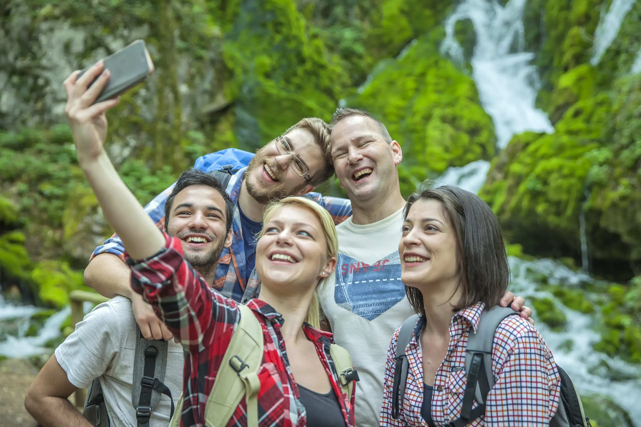 Gruppo di viaggiatori sorridenti che si scattano un selfie davanti a una cascata. Viaggi avventura di gruppo Monica Alberghini.
