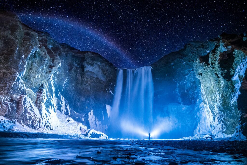 Cascata Skógafoss in Islanda illuminata di notte sotto un cielo stellato con arcobaleno lunare