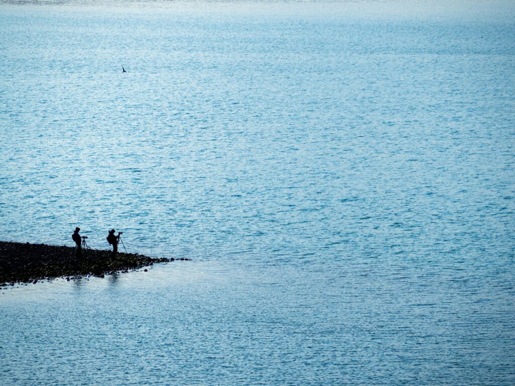 Due fotografi sulla riva di un lago in Islanda, ripresi in controluce contro le acque azzurre
