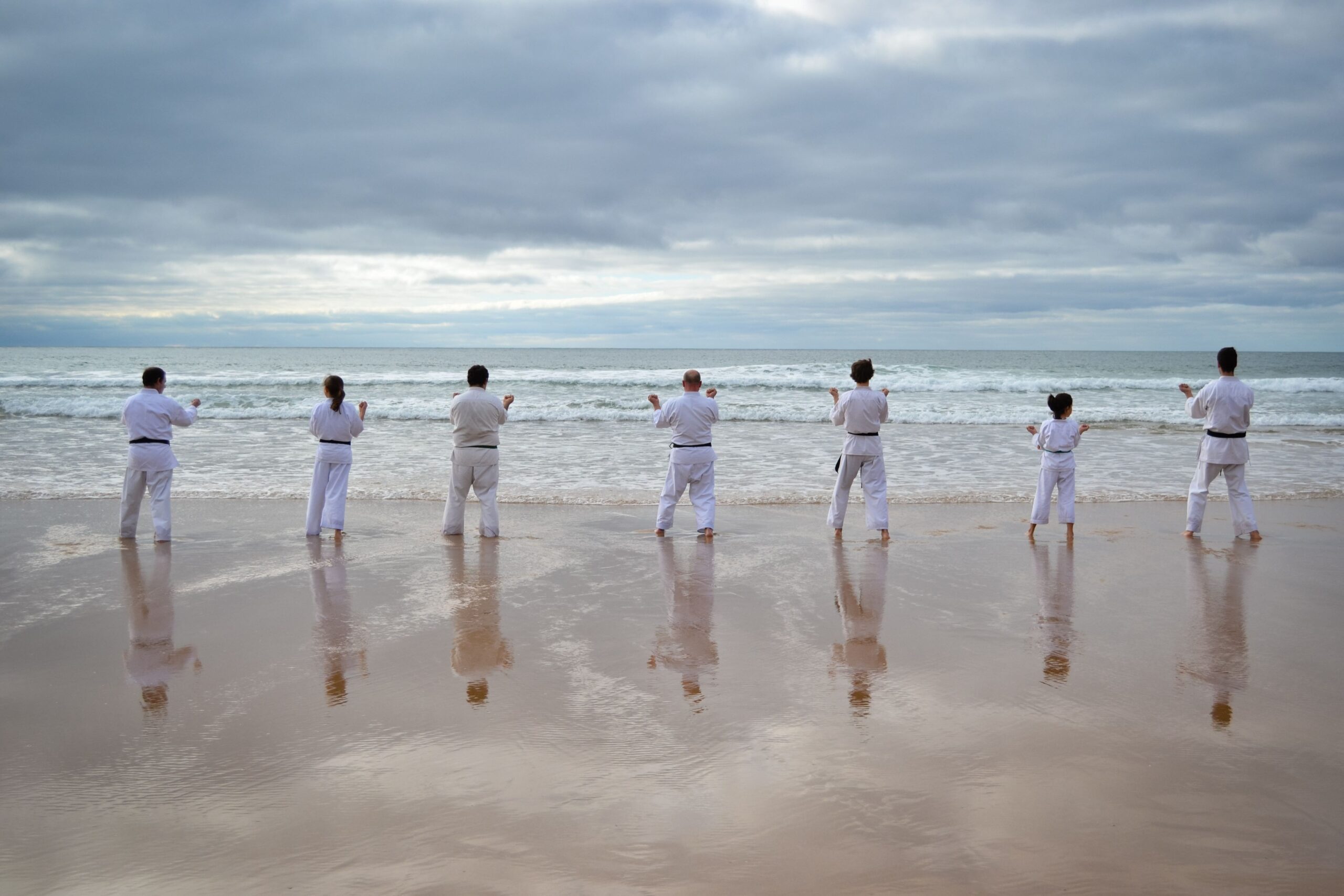 Gruppo di persone in divisa da karate che pratica arti marziali sulla spiaggia durante un'attività di team building aziendale